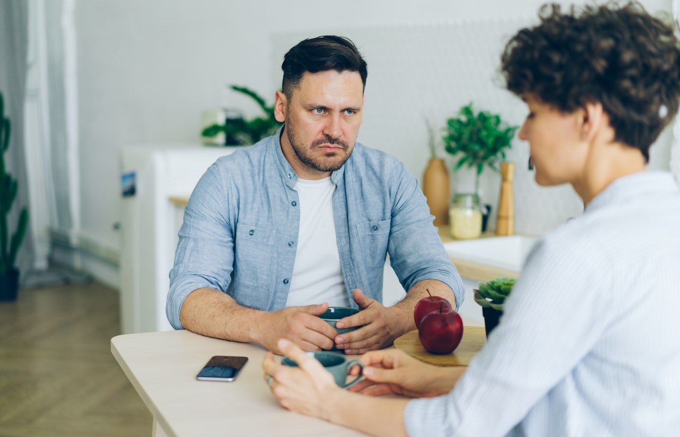 Two people having a serious conversation across a kitchen table over coffee